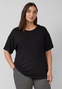 Czarny T-shirt z krótkim rękawem i okrągłym dekoltem, charakteryzujący się miękką teksturą i subtelnym, kropektowym wzorem na tkaninie. Połączony z szarymi spodniami.