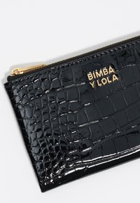 Cartera de cuero sintético negro con textura de relieve de cocodrilo, que presenta un logotipo dorado, cierre de cremallera y esquinas redondeadas.