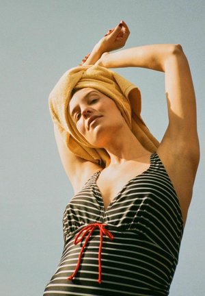 Sort-hvid stribet badedragt med en rød snor, parret med et gult håndklæde om håret mod en lyseblå baggrund.