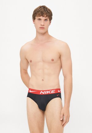 Schwarze Herrenunterwäsche mit einem roten Nike-Logo-Bund. Der Stoff ist glatt, und das Design verfügt über einen klassischen Schnitt mit minimaler Bedeckung.