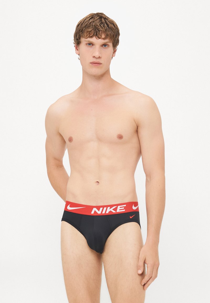Black men's briefs with a red Nike logo waistband. The fabric is smooth, and the design features a classic cut with minimal coverage.