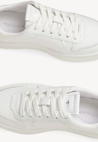 Vita sneakers med en slät läderöverdela, rund tå och platta snörningar, med en strukturerad sula och diskret logotyp på tungan.