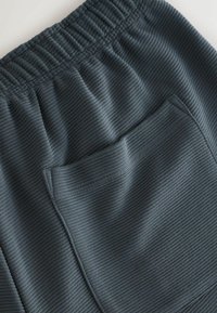 Ciemnoszare, prążkowane spodnie dresowe z elastycznym pasem i boczną kieszenią, prezentujące teksturowaną tkaninę z pionowymi paskami.