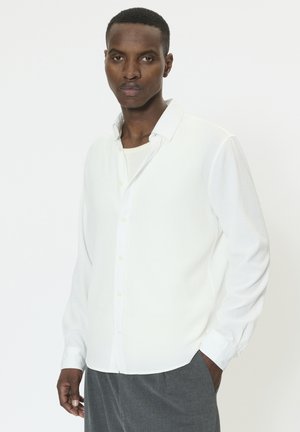 Weißes, strukturiertes Langarmhemd mit einem Button-Down-Kragen und einer Frontleiste, kombiniert mit grauen Hosen, mit einer lockeren Passform.