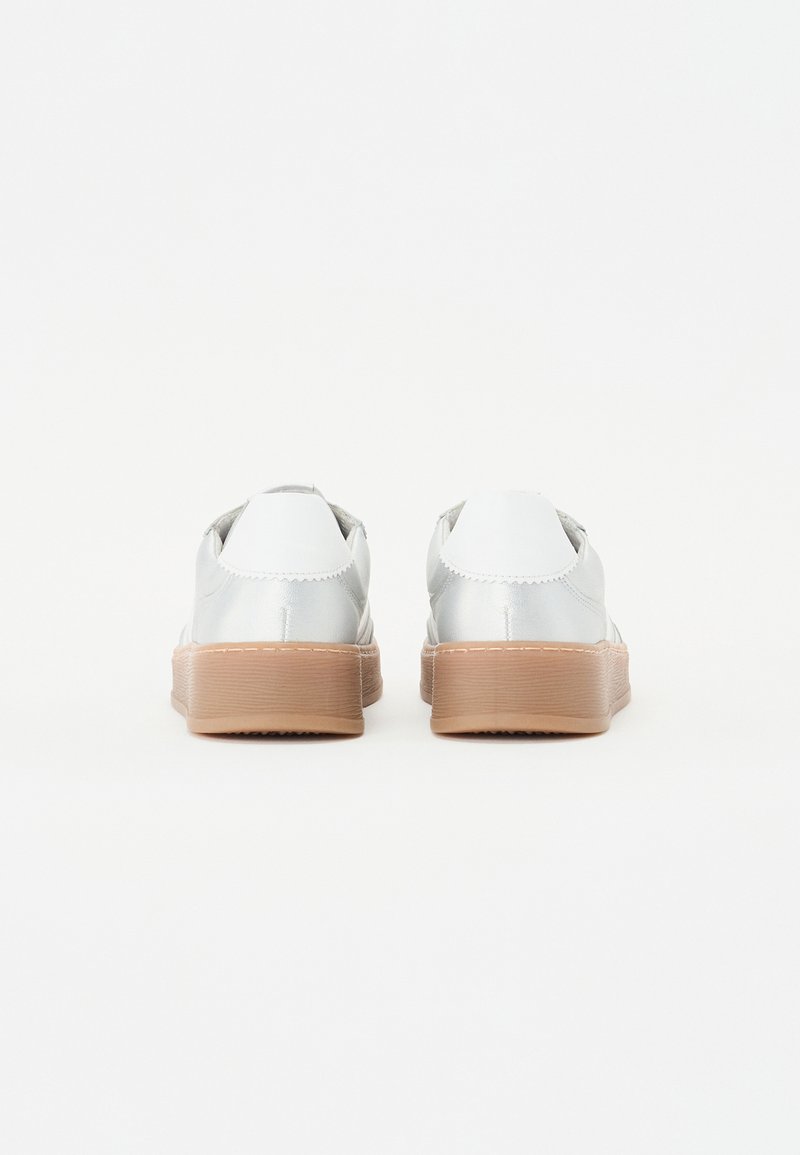 Silberne Sneakers mit einer glatten, metallischen Oberfläche, die beige Gummisohlen und genähte Details entlang der Kanten aufweisen. Rückansicht gezeigt.