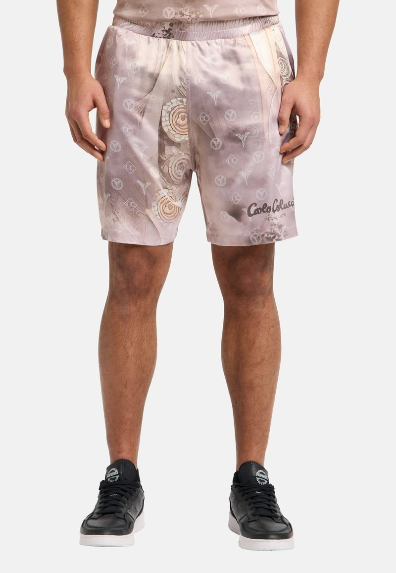 Lyserøde satiny-shorts med et svunget mønster og logo-detalje. Elastisk talje og sidelommer. Sammen med sorte sneakers.