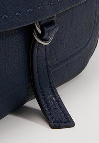 Granatowa skórzana torebka zbliżenie, z fakturowaną powierzchnią, metalowymi elementami i wyszywanym paskiem skórzanym z prostokątnym zakończeniem.