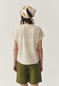 Crème-kleurig korte mouwen shirt met bloemenborduurwerk, gecombineerd met olijfgroene shorts. Het shirt heeft een ronde zoom en een losse pasvorm.