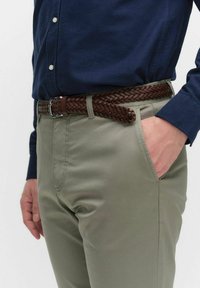 Flätad brun läderbälte bärs över ljusgrå byxor, tillsammans med en marinblå skjorta med knappar. Synliga sömdetaljer på byxorna.