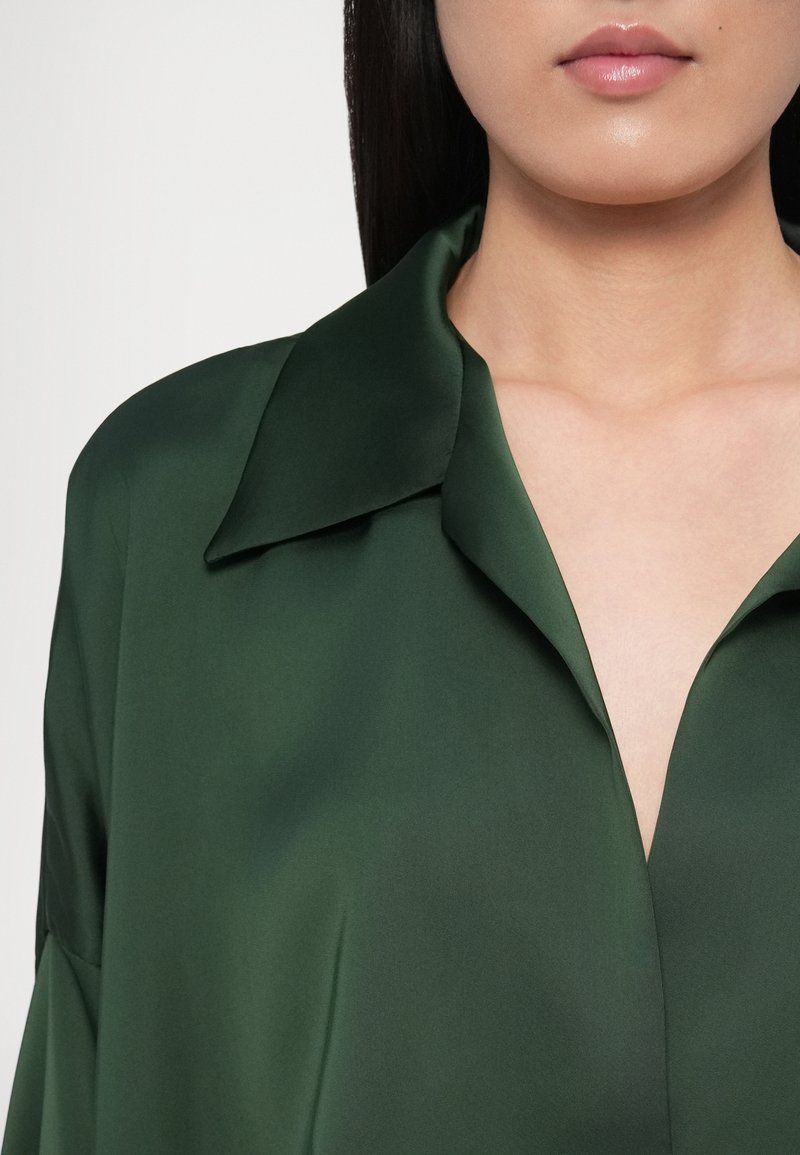 Dark green silk shirt with a wide collar, featuring a smooth texture and a subtle sheen, displaying a V-neck cut.