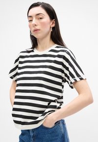 Tricou cu dungi alb-negru, cu mâneci scurte și guler rotund, prezentat cu o croială relaxată. Textura pare netedă și similară cu bumbacul.
