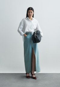 Sac à main noir en tricot, chemise boutonnée blanche rayée, jupe en jean taille haute avec une fente devant, et talons à bride cheville bordeaux.