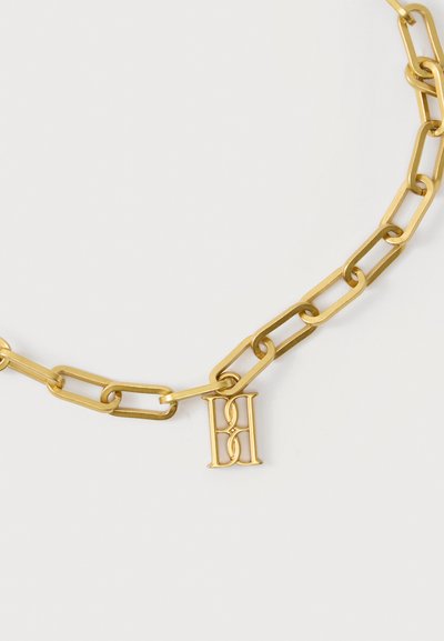 Χρυσό κολιέ αλυσίδα με μεγάλα ορθογώνια κρίκια και μενταγιόν που απεικονίζει διασταυρούμενα γράμματα "B" και "H" σε φωτεινό φόντο.
