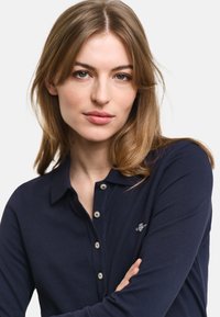 Tengerészeti hosszúujjú polo ing gombos nyakkal, kisméretű logóval a mellrészen. Az anyag textúrázott kötött mintával bír.