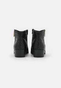 Ein Paar schwarze Knöchelstiefel mit Krokodiltextur und goldenen Reißverschluss-Zipper, von hinten auf einem weißen Hintergrund betrachtet.