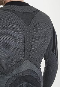 Svart och grå långärmad tröja med texturerad meshväv, som har geometriska mönster och en figurnära design för atletisk användning.