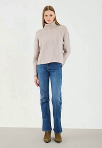 Ljust beige ribbade polotröja, kort design, ihopparad med blå utsvängda jeans och olivgröna stövletter. Slen textur, avslappnad stil.
