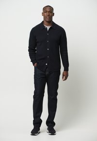 Cardigan de punto en navy oscuro con cierre de botones, camiseta gris, jeans oscuros y zapatillas negras. Cuello sencillo y detalles de textura acanalada.