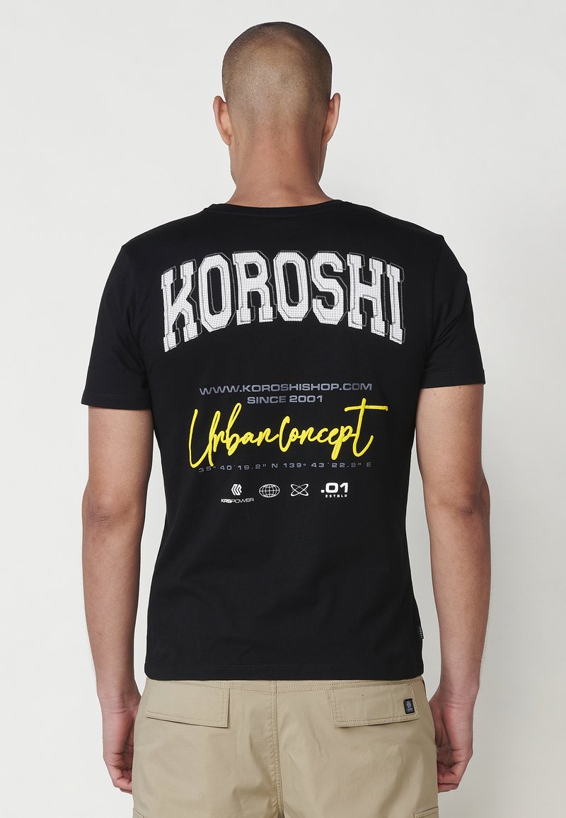 Camiseta de algodón negra con gran texto blanco "KOROSHI" y un gráfico amarillo "Urban Concept" en la parte trasera con múltiples detalles y coordenadas.