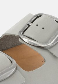 Light gray suede sandal featuring a large metallic buckle and open cutouts, with a natural leather insole and textured edges.