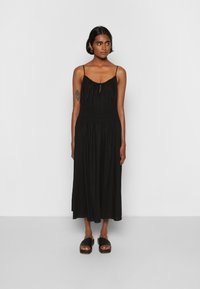 Vestido maxi preto com cintura ajustada, alças finas ajustáveis e uma silhueta solta e fluida. Combinando com sandálias plataforma pretas.