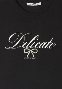 Czarna bawełniana koszulka z napisem "Delikatne" w białym kolorze, ozdobionym perłową kokardą, oraz napisem "PUNKT WIDZENIA" poniżej w bieli.