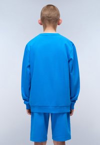 Completo in felpa blu e pantaloni corti, realizzato in tessuto morbido. Presenta una vestibilità comoda, polsini a coste e un design monocolore senza fantasie.