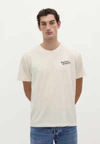 Beige bomulds T-shirt med rund halsudskæring, korte ærmer, og et brunt logo med teksten "Sealperso Company" på venstre bryst.