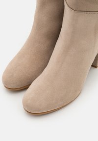 Bottines en suède beige avec un bout pointu et un talon bloc. La surface a une texture douce avec peu de détails de couture.