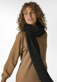 Sort tørklæde med en tekstureret, glitrende finish, båret løst om halsen, som står i kontrast til en lysebrun sweatshirt.