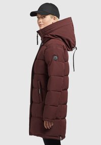 Bordo nadýchaná bunda s veľkou kapucňou, dvoma bočnými vreckami a čiernymi zipsovými akcentmi. Styling s čiernou čiapkou. Vyrobená z hrubého, zatepleného materiálu.