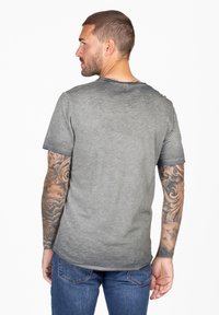 Camiseta gris de manga corta con cuello redondo, que presenta una textura sutil y un dobladillo recto. Combinada con pantalones vaqueros de denim azules.