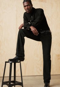 Zwarte denim blouse en broek, met een gladde textuur, getailleerd ontwerp en een lichte glans. Zwarte leren laarzen met een blokhak.