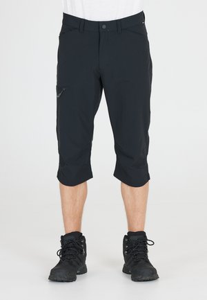 Svarta knälånga shorts i lätt material, med en zippered sidficka och uppvikta ärmar. Bärs med svarta vandringsskor.
