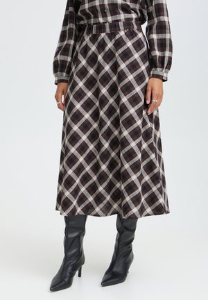 Femme portant une jupe à carreaux marron et blanc avec un chemisier assorti à carreaux et des bottes noires à talons aiguilles pointues.