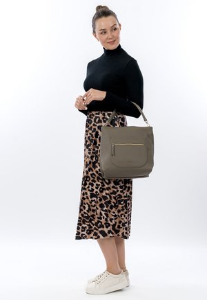 Olive green leather handbag with a front zip pocket, paired with a black turtleneck and leopard print skirt, alongside white sneakers.