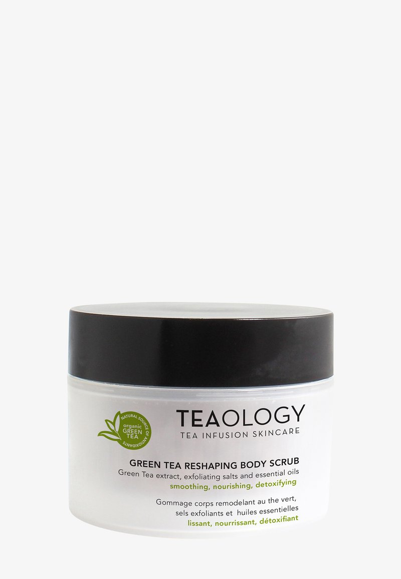 Barattolo di plastica trasparente con coperchio nero. L'etichetta mostra "TEAOLOGY Green Tea Reshaping Body Scrub" con accenti verdi e testo in più lingue.