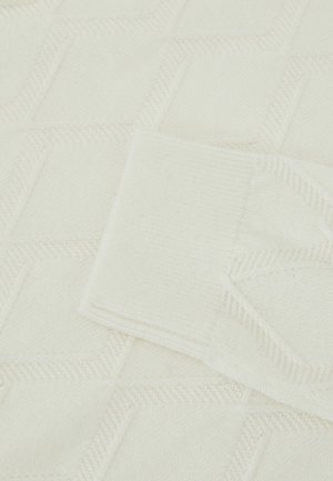 Kremfarvet strikket stof med et tekstureret geometrisk mønster og en opsmøgget kant i en glat strik. Blødt og varmt stof generelt.