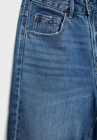 Siniset farkut, joissa on keskirusketus, perinteinen viiden taskun malli, hillitty kulutusefekti ja vähäistä kulumista etutaskuissa.