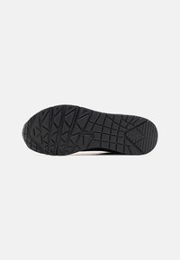 Black sneaker sole with a textured rubber grip pattern, featuring geometric shapes and deep treads for traction and durability.