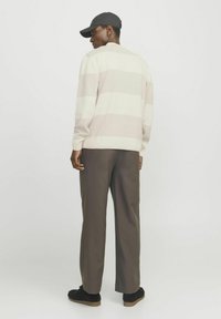 Pullover i creme med lyserøde striber, ribbede manchetter og nakkesnit på ryggen. Bærer sammen med mørkebrune bukser og sorte sneakers.