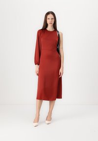Czerwona midi sukienka z jedną długą balonową rękawą, dopasowanym korpusem i elegancką sylwetką. Gładki materiał o minimalistycznym designie i czarnym akcentującym pasku.