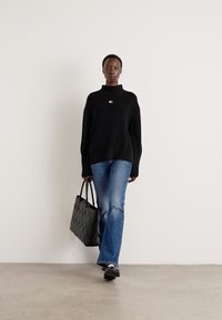 Svart oversized strikkegenser med høy krage, sammen med blå utsvingte jeans. Holder en strukturert svart toteveske. Enkle sko.