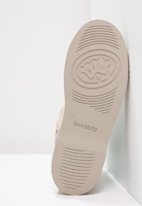 Beige sko sula med räfflad textur, med en cirkulär logo och varumärket "SHABBIES" präglat. Storlek markerad som "37."