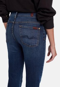 Vaqueros de mezclilla azul oscuro con corte ajustado, que presentan bolsillos traseros, detalles de costura y una pequeña etiqueta de marca en la cintura.