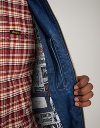 Τζάκετ τζιν με κόκκινη και λευκή καρό επένδυση. Ο εσωτερικός χώρος διαθέτει εκτυπωμένα γραφικά με λογότυπα συγκροτημάτων. Χρυσός φερμουάρ και ραμμένες λεπτομέρειες.