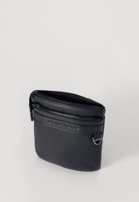 Pochette in pelle nera con texture liscia, dotata di chiusura con zip superiore e di un logo decorativo. Design minimalista, forma compatta e portatile.