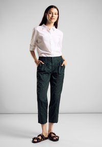 Vit skjorta med uppvikta ärmar, tillsammans med mörkgröna, elastiska capribyxor. Skorna är svarta och bruna med leopardmönster.