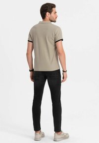 Khaki polo tričko s černým lemem, v kombinaci s černými džíny. Tričko má klasický límeček a volný střih; džíny jsou slim-fit.