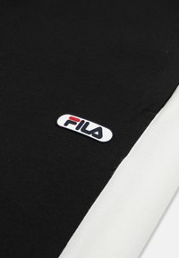 Zwart-witte stof met een klein FILA-logo patch met rode en marineblauwe letters op het zwarte gedeelte.